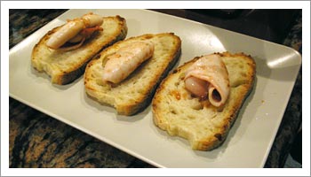 Prepara le bruschette disponendo un totano sulla superficie non tostata di ogni fetta di pane.