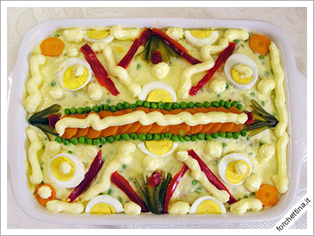Aggiungi la maionese sulla superficie, e infine per guarnire, i piselli, le carote, i cetriolini e le uova sode tagliate logitudinalmente.