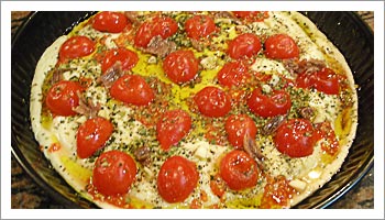 Aggiungi i pomodori Tagliati in due e disponili casualmente sulla superficie. Aggiungi pezzetti di alici sfilettate, l'aglio 
tagliato a pezzettini.