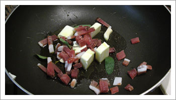 Aggiungi i pezzi di speck tagliati a dadini, l'aglio e le foglie di 

salvia