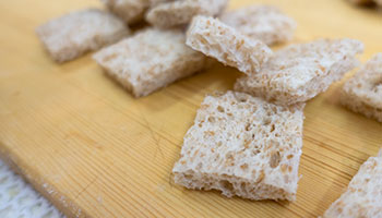 Taglia in quattro parti ogni fetta di pane e disponi su di una teglia foderata con carta forno.